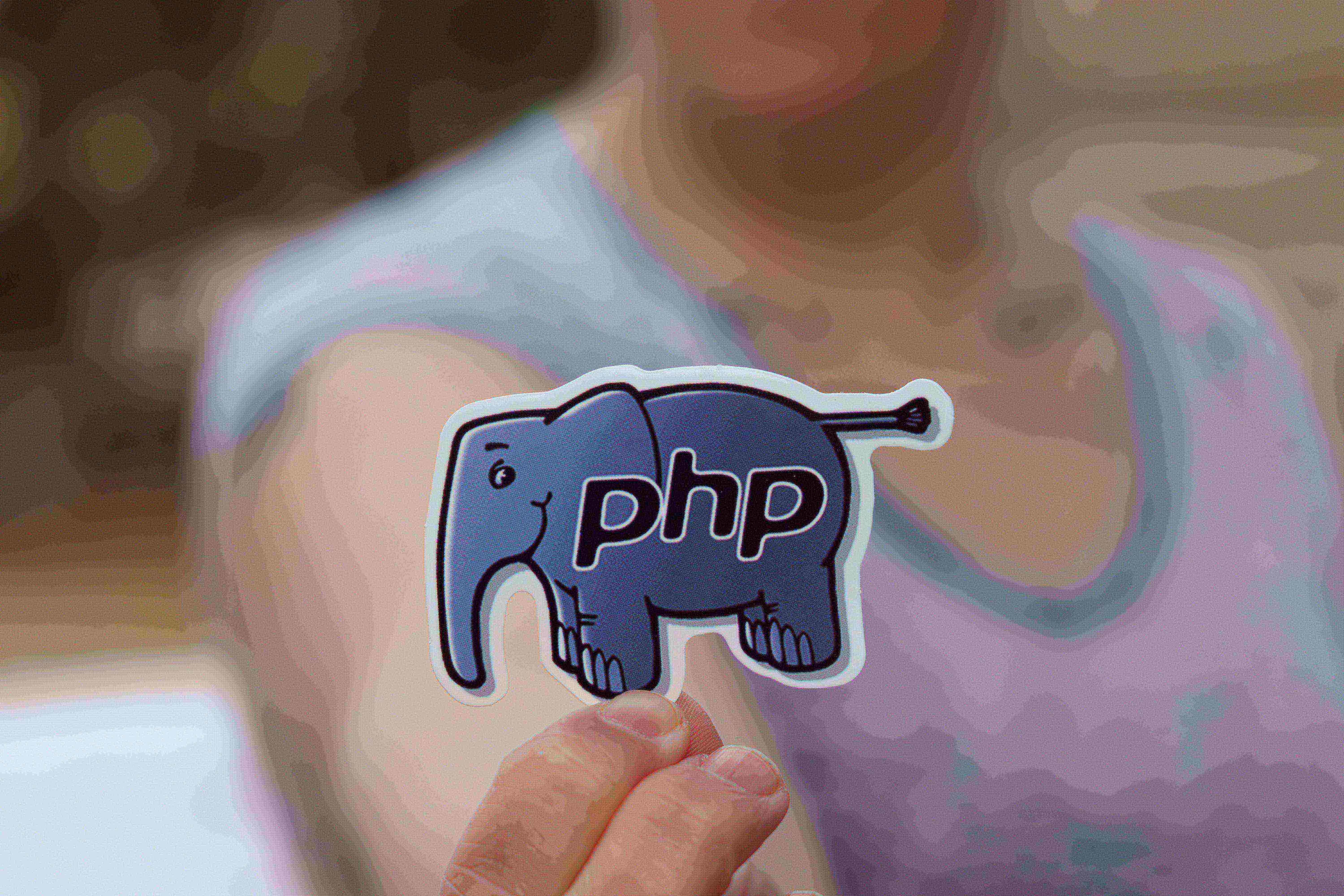 Homem segura um adesivo em formato de elefante, dentro dele as iniciais de 'PHP',
         pois o elefante é considerado mascote desta linguagem de programação. 